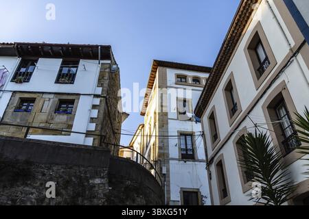 Sunlight illuminates the walls of two buildings, one whitewashed, the other stone, in a narrow street. Lastres, Asturias Stock Photo