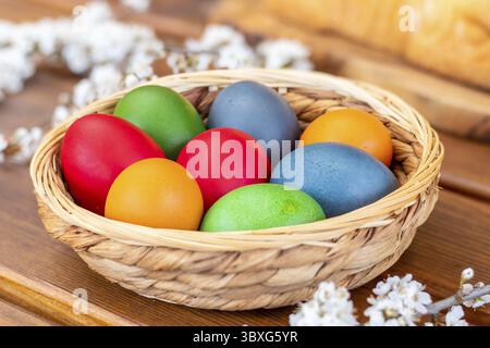 Easter eggs, dyed hen eggs in a wicker basket bowl on wooden table Stock Photo