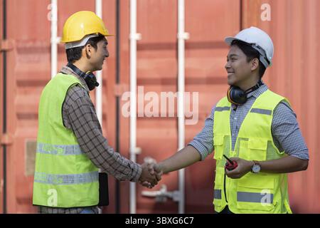 Two professionals in safety vests and helmets shake hands, symbolizing teamwork in logistics and engineering within a construction site Stock Photo