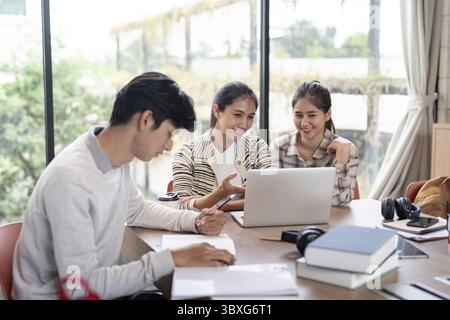 A group of students working together on a project in a bright, modern study area, using laptops and books for research and collaboration Stock Photo