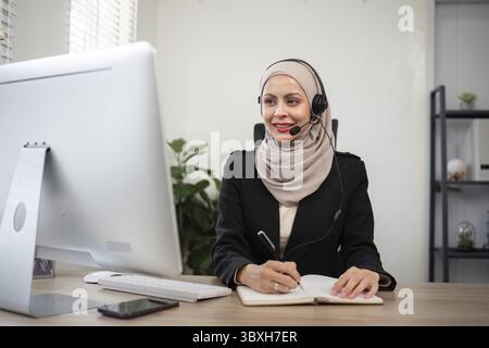 Young muslim women wearing hijab telemarketing or call center agent with headset working on support hotline at office Stock Photo