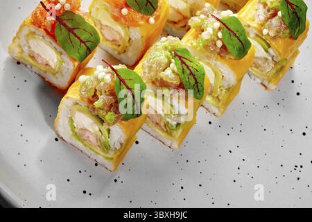 Sushi rolls with omelette, shrimp, avocado, and tobiko, decorated with herbs, served on a plate Stock Photo