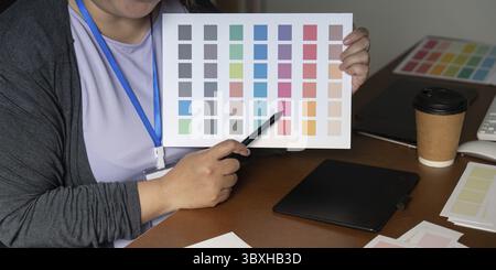 A graphic designer holds a colorful palette sheet, pointing out key colors for upcoming projects, highlighting the importance of color in visual desig Stock Photo