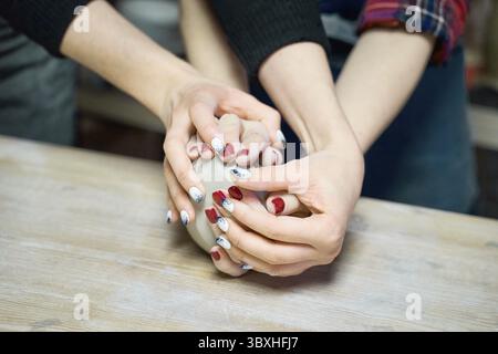Woman making ceramic pottery, four hands close-up, focus on potters, palms with pottery, concept for workshop and master class Stock Photo