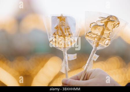 Hand holding Christmas golden lollipops candy on stick. Stock Photo