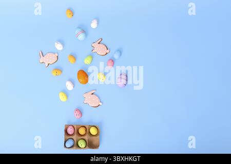 Decorative multicolored eggs and pink gingerbread in the form of rabbit, scattered on a light blue background, top view. Copy space Stock Photo