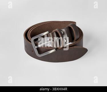 Custom dark brown genuine leather belt with stylish matte buckle and DAD embossing, folded on white background. Concept of quality craftsmanship and p Stock Photo