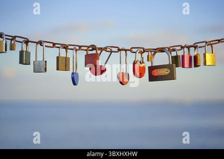 Various and heart colorful shaped love padlocks on a chain on a beautiful blue sky and sea background. Diverse locks as a symbol of togetherness and b Stock Photo
