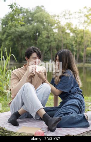 A young couple having a picnic in a park, sharing food and enjoying each other's company amidst a serene natural setting Stock Photo