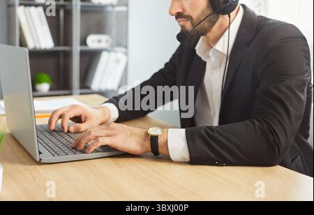 Call center operator in headset working on laptop, communicating with clients in office Stock Photo