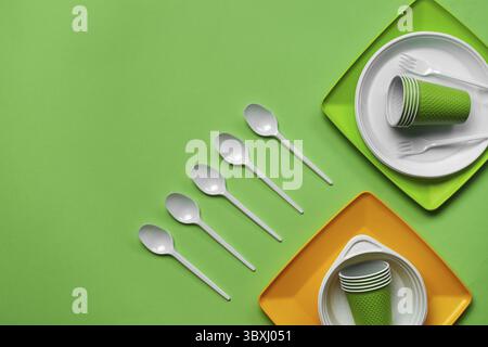 Colorful plastic disposable cutlery, such as plates, five spoons, two forks and bowls on green background with copy space. The concept of picnic utens Stock Photo