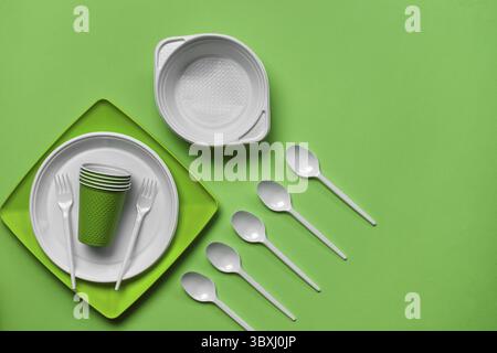 Colorful plastic disposable tableware, such as plates, five spoons, two forks and bowls on green background with copy space. The concept of picnic ute Stock Photo