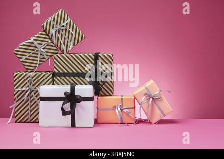 Different sized, colorful, striped and plain, brown, rose and white paper gift boxes tied with colored ribbons and bows on a pink surface and backgrou Stock Photo