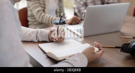 Students collaborating on a project, using laptops and notebooks, in a modern classroom environment Stock Photo