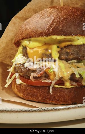 Double burger with melted cheese, crispy bacon, fresh lettuce, tomato slices, and dripping sauces, served on a plate Stock Photo