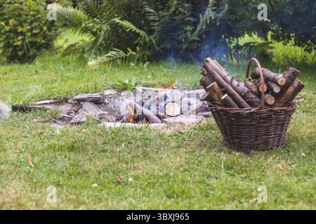 Camp fire in the garden, next to a basket with firewood Stock Photo