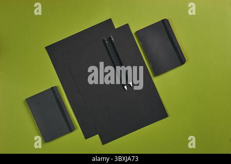 Two sheets of black paper, pencils and folders on green background with copy space. Education, workplace concept. Top view in focus with different off Stock Photo