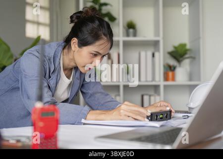 A dedicated engineer uses a precision tool to measure blueprints, demonstrating focus and attention to detail in a modern office setting Stock Photo