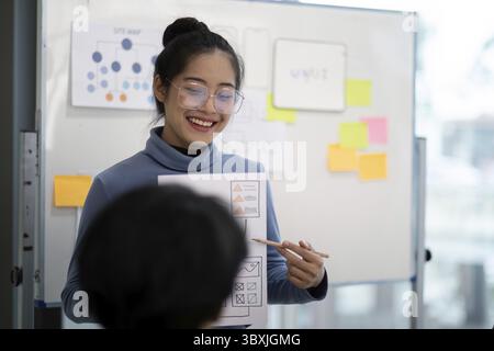UX developer and UI designer collaborating on project ideas, using wireframes and flowcharts on a whiteboard in a modern office setting Stock Photo