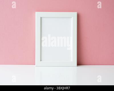 Blank white frame on a white table against the pink wall with copy space Stock Photo
