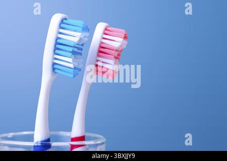 Close-up of blue and red toothbrushes in glass on blue background Stock Photo