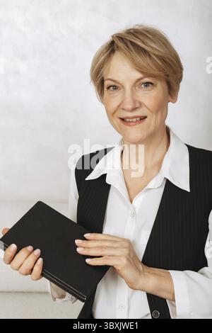 Portrait of business woman. Confident, successful mature woman holding black diary on light gray background. Looking at camera. Stock Photo