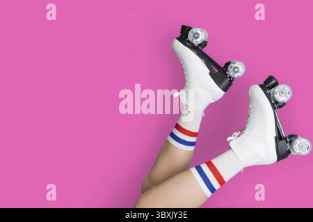 Retro white roller skates on legs with striped socks against pink background Stock Photo