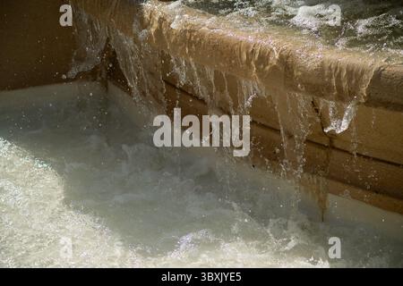 Clear water falls rapidly from the side of the beige marble fountain Stock Photo