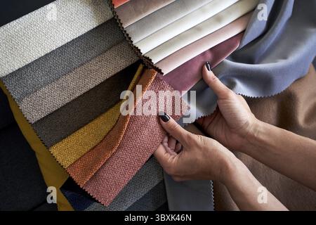Choosing upholstery fabric color and texture from various colorful samples in a store. Female customer hands touching textile Stock Photo