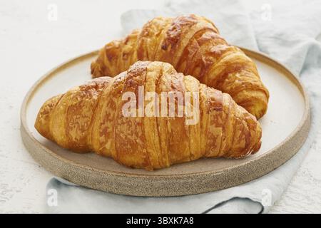 Two delicious croissants on a plate and a hot drink in a mug. Morning French breakfast with fresh pastries. Light gray background Stock Photo