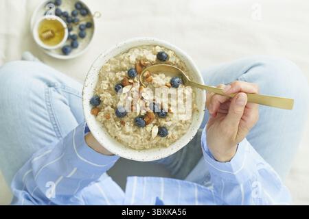Top view faceless woman holding plate of oatmeal, sitting in bed early morning, quiet home environment. Healthy breakfast Stock Photo