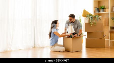 Excitement fills the air as a couple unpacks moving boxes in their cozy living room. They share smiles while organizing their new space, eager to crea Stock Photo