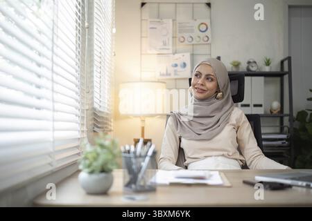 Smiling Muslim woman sitting at office desk. Professional workspace, casual attire Stock Photo