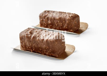 Two appetizing nuts and chocolate covered ice cream bars presented on golden serving cardboards on white background, perfect for sweet treat Stock Photo