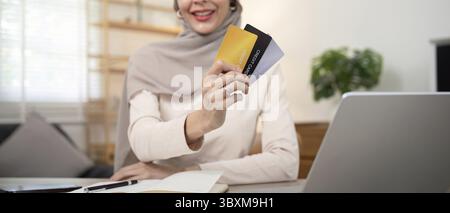 Young woman using laptop at home shopping online. Muslim woman wearing hijab using laptop and holding credit card. Internet banking concept. Muslim wo Stock Photo