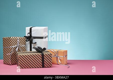 Various sized, striped and plain, brown, pink and white paper gift boxes tied with black and silver ribbons and bows standing on a pink surface and bl Stock Photo