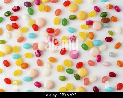 Many scattered colorful sweets, candies, lollipops on white background, top view. Jelly beans Stock Photo