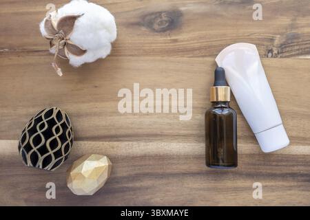 Easter spa. Hand and face cream and oil in glass bottle on wooden background. Golden and black eggs of geometric style. Happy Easter greeting card. Stock Photo