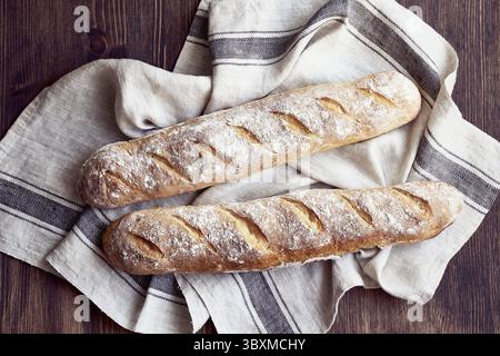 Fresh baked homemade crusty french baguette. Two loaves on linen towel on wooden table. Delicious and healthy homemade cakes Stock Photo