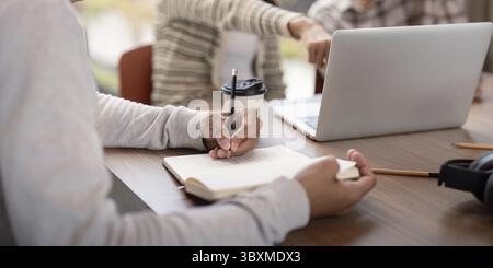 Students engaged in collaborative study session, using laptops and notebooks in a modern classroom environment Stock Photo