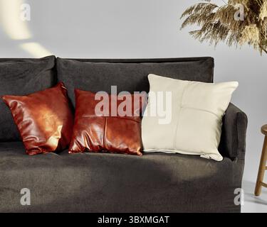 High-end brown and cream leather pillows arranged on modern dark grey sofa in chic interior of living room Stock Photo