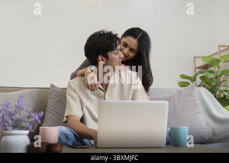Young couple asian using laptop together while sitting on sofa at home Stock Photo