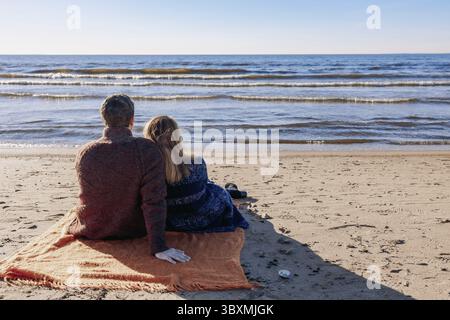 Loving couple walks on beach along sea on sunny autumn day. Weekend and lifestyle concept. Back view. Stock Photo