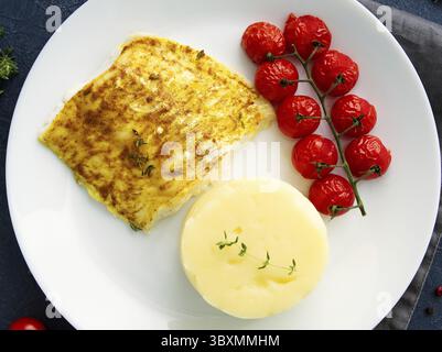 Fish cod baked in the oven with mashed potatoes, tomatoes, diet healthy food. Dark gray background, top view Stock Photo