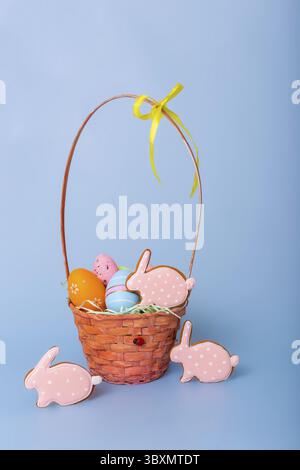 Three pink gingerbread in the form of a rabbit and a basket with decorative Easter eggs stand on a blue background Stock Photo