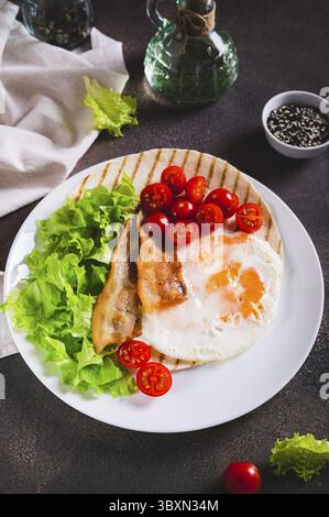 Food, Grilled tacos with egg, fried bacon, vegetables and herbs on a plate on the table vertical view Stock Photo