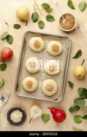 Food, Raw homemade buns made of yeast dough with jam and fresh pears. Mini pies. Cooking recipe on a wooden background. Top view Stock Photo