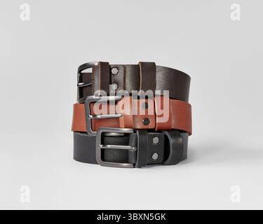 Closeup of three folded leather belts of different colors with DAD embossing on loops against white background. Stylish personalized handcrafted acces Stock Photo