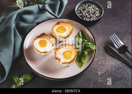 Food, Baked egg and bacon rolls with basil on a plate on a table Stock Photo