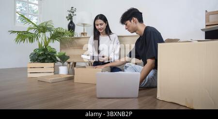 A young couple unpacks boxes in their new home, surrounded by plants and modern decor, symbolizing a fresh start and new beginnings Stock Photo